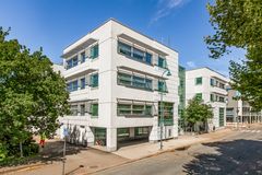 Valkoinen, kolmikerroksinen moderni rakennus, jossa on leveät ikkunat, sijaitsee kesäisessä ympäristössä.