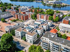 Ilmakuva urbaanista alueesta, jossa on tiiviisti sijoitettuja rakennuksia, puita ja vesistö taustalla.