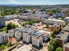 Ilmakuva kaupunginosasta, jossa näkyy useita kerrostaloja ja pysäköintialue. Taustalla on merinäkymä.
