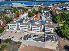 Ilmakuva valkoisesta rakennuksesta, jonka katolla on lasisia kattoikkunoita. Taustalla näkyy lisää rakennuksia ja vesistö.