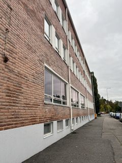 Kolmikerroksinen tiilirakennus kadun varrella, pilvinen taivas.