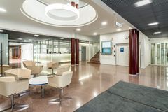 Avara ja valoisa toimiston aula, jossa on beigejä tuoleja, pyöreitä pöytiä ja moderni sisustus. Taustalla on vastaanottotiski ja portaat.