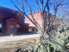 Vanha punatiilinen kasarmirakennus keväisessä säässä. Etualalla näkyy vanha tykki ja lehtipuu ilman lehtiä.