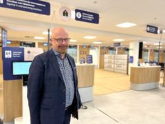 Henkilö seisoo modernissa aula-alueessa. Taustalla opasteita ja palvelutiskejä.