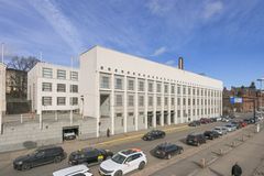 Valkoinen, modernistinen rakennus kadun varrella, jossa on autoja pysäköitynä.