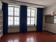 Tyhjä huone, jossa on punainen lattia, kaksi suurta ikkunaa ja siniset verhot.