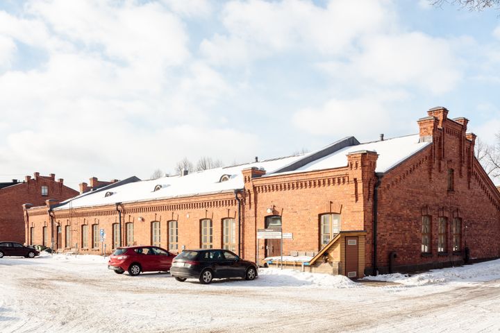 Lumipeitteinen punatiilinen teollisuusrakennus, jonka edessä on pysäköitynä autoja.