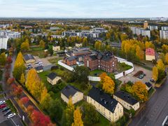 Ilmakuva syksyisestä kaupunkimaisemasta, jossa on puita, kerrostaloja ja tiilirakennus.