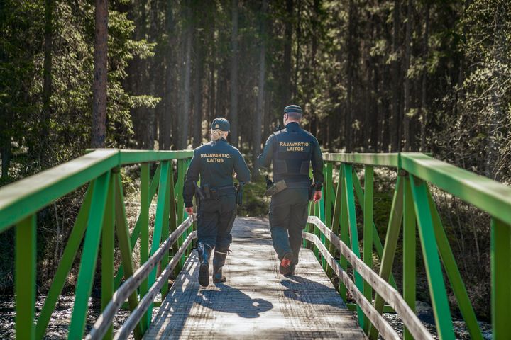 Kaksi henkilöä kävelee vihreällä sillalla metsässä. Heidän univormuissaan lukee "RAJAVARTIOLAITOS".