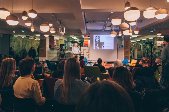 Ihmisiä yleisössä kuuntelemassa luentoa.