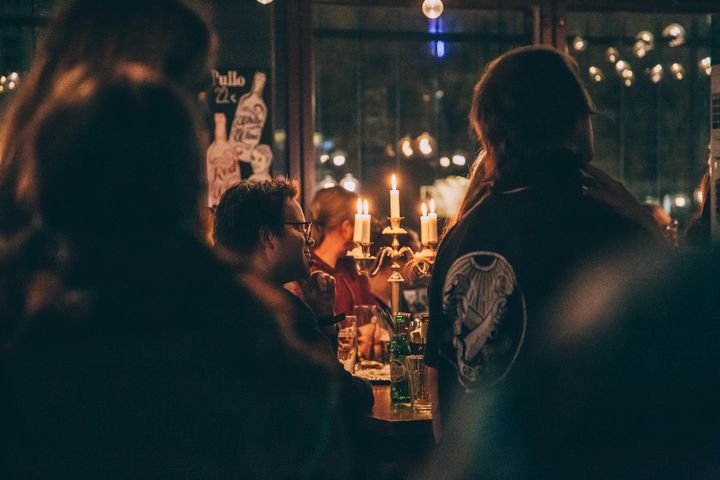 Hämärä valaistus täydessä baaritilassa, pöydällä kynttilöitä, ihmiset kuuntelevat.