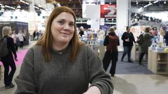 Nainen hymyilee, ympärillä messuhälinää, ihmisiä ja kirjahyllyköitä.