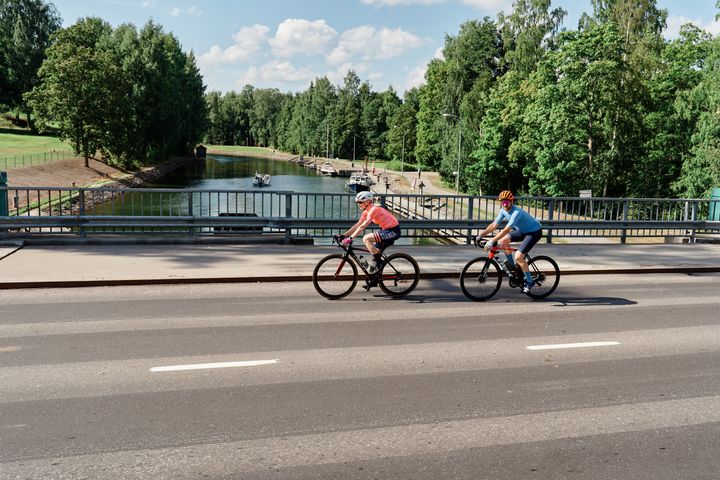 Kaksi pyöräilijää pyöräilemässä ajotiellä. Takana kanava.