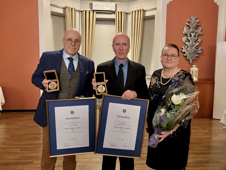 Kolme ihmistä ryhmäkuvassa, kahdella on käsissään Päijät-Häme-mitalit ja kunniakirjat, kolmannella kukkakimppu.