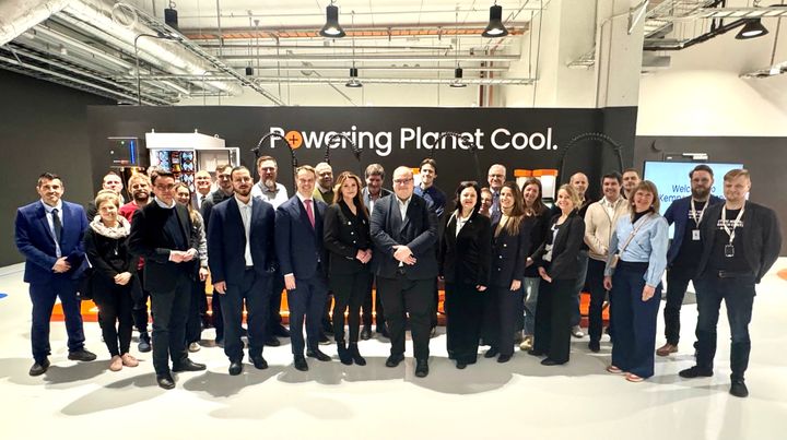 Ryhmäkuvassa noin 30 henkilöä sisätilassa. Taustalla seinässä teksti: Powering Planet Cool.