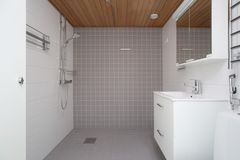 Tilava kylpyhuone, jossa on harmaa laatoitettu seinä, suihku ja valkoinen allaskaappi.