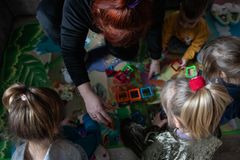 Nainen leikkii kolmen lapsen kanssa lattialla lelujen parissa.