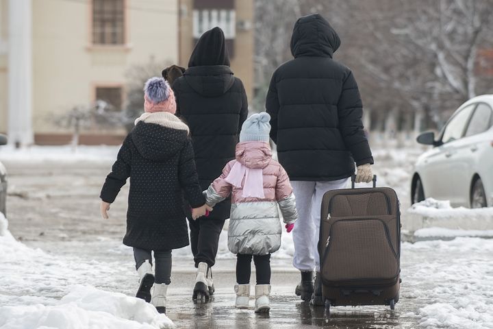 Perhe kävelee selin kameraan kadulla. Aikuisen vetää perässään matkalaukkua.