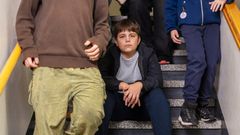 Poika istuu rappusilla ja katsoo kameraan. Ympärillä muut laskeutuvat portaita alas.