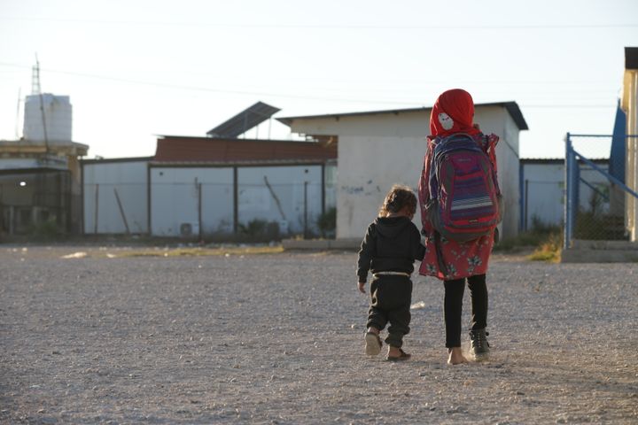 Lapset kulkevat selin ja käsikädessä pakolaisleirillä.