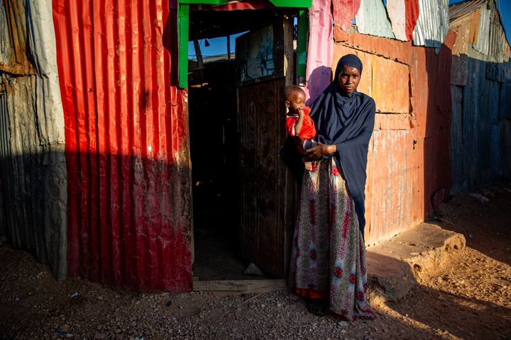 Nainen seisoo ulko-oven edessä Somalian Puntmaassa, pitäen lasta sylissään.