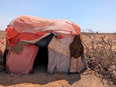 Nainen seisoo vaatimattoman majan edessä rutikuivassa maastossa.