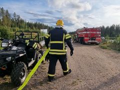 Sopimuspelastaja vetää paloletkua hiekkatiellä. Taustalla paloauto.