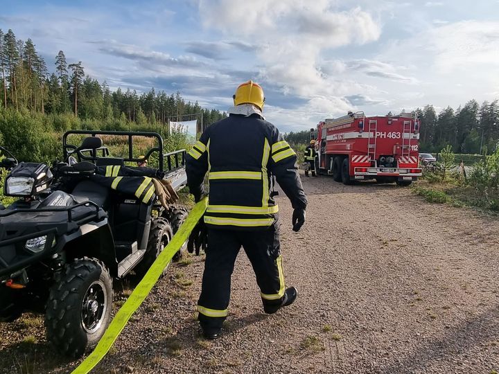 Sopimuspelastaja vetää paloletkua hiekkatiellä. Taustalla paloauto.