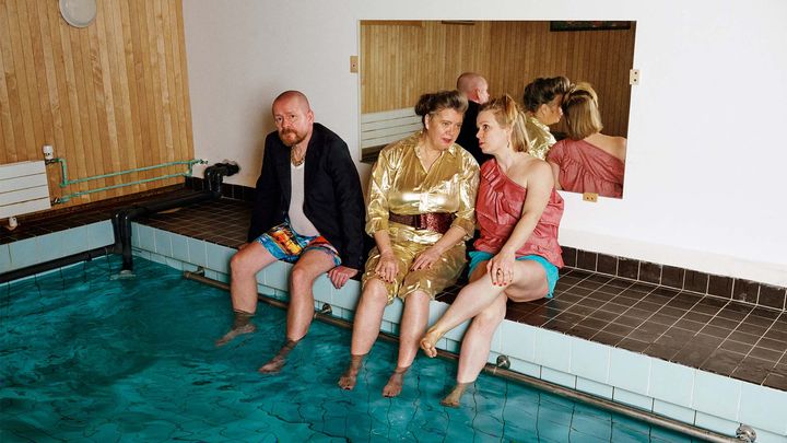 Kolme ihmistä istuu uima-altaan reunalla.