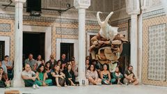 Kuvassa on tanssiesitys, jossa esiintyjä hyppää ilmassa, ja yleisö seuraa esitystä istuen salissa.