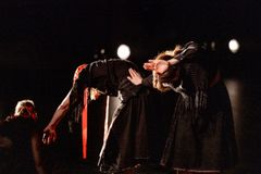 Kaksi henkilöä taipuvat eteenpäin tummissa vaatteissa pimeässä tilassa.