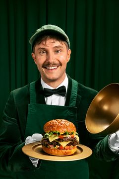 Hymyilevä Mr. Frebu pitelee tarjottimella Friends & Brgrsin hampurilaista kultaisen tarjoilukuvun kanssa.