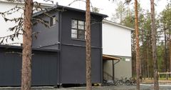 Moderni kaksikerroksinen rakennus metsän reunalla, pyöriä nojaa seinää vasten.