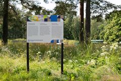Infotaulu luontotyöstä niityllä puiden keskellä.