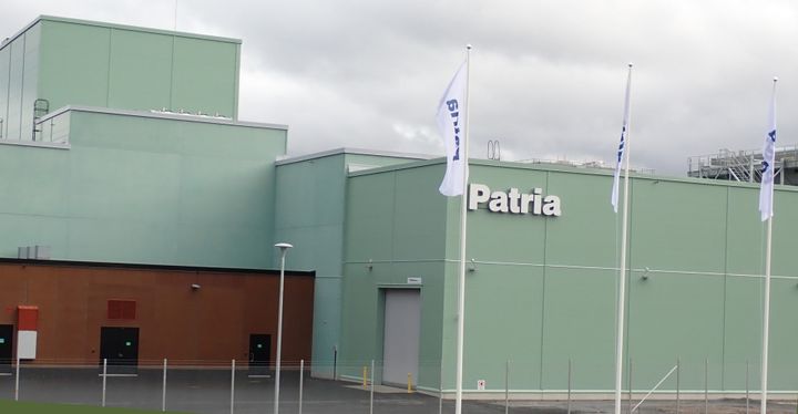 Alt-teksti: Tuotantotila, seinässä Patria-logo ja liehuvia lippuja edessä.