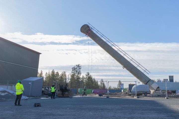 Vanhan lämpölaitoksen korkea piippu kaatumassa maahan kirkkaana päivänä.