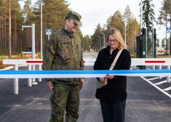 Nainen leikkaa sinisen nauhan virkapukuisen miehen vieressä.