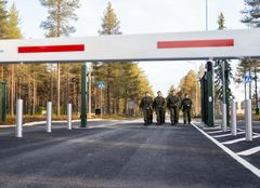 Sotilaat kävelevät maantiellä portin lähellä metsäisessä ympäristössä.