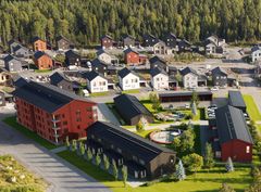 Ilmakuva asuinkorttelista, jossa on punaisia ja tummia kerrostaloja sekä pienempiä rakennuksia, ympärillä vehreää aluetta ja metsää.