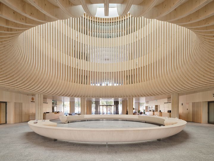 Träkonstruktionerna som böjer sig i en båge uppåt ovanför den öppna hallen skapar en unik stämning som bjuder in besökaren att sätta sig på bänken som har formen av en stor cirkel, beskriver Luoma i sina prismotiveringar.