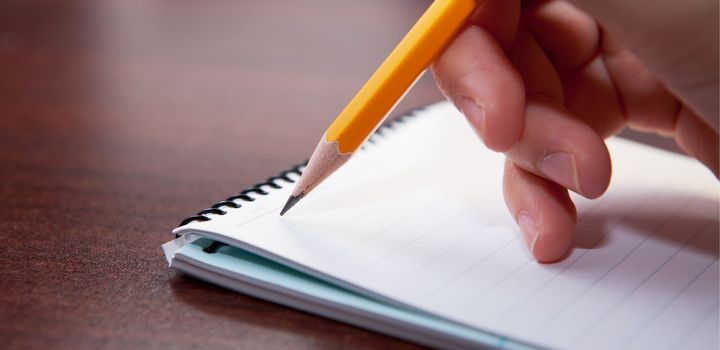 Käsi kirjoittaa lyijykynällä muistiinpanoja muistikirjaan.