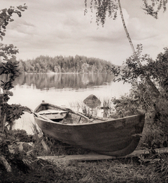 Valokuva venerassa, jossa on puinen soutuvene. Taustalla järvi sekä horisontissa järven takana metsää.