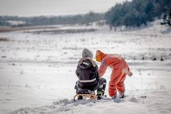 Lapset rattikelkan kanssa talvisessa maisemassa.