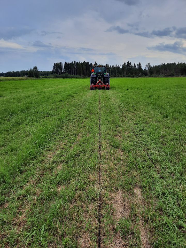 Traktori jankkuroi vehreää peltoa loppukesän maisemassa.