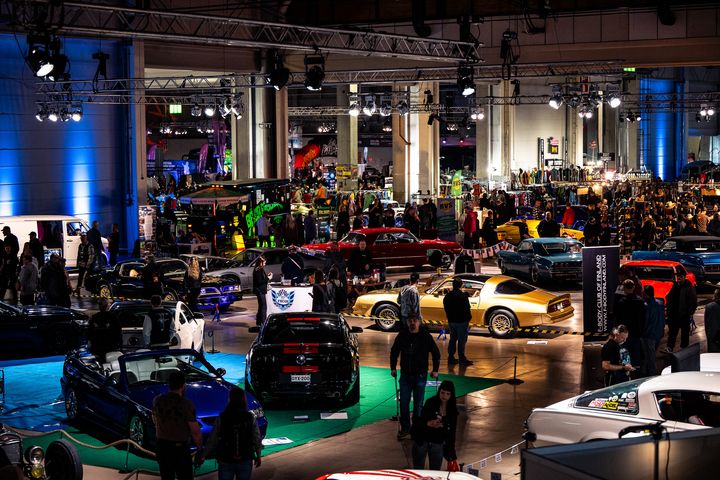 Autonäyttely, jossa on monia erimallisia ja -värisiä autoja valaistussa hallissa.