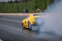 Keltainen auto tekee burnoutin radalla, tuottaen paljon savua.