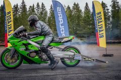 A motorcycle rider in racing gear on a green bike, with colorful banners in the background.