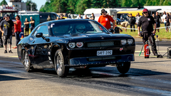 Dodge Challenger -auto kiihdytyskilpailussa, etupyörät ilmassa. Yleisöä taustalla.