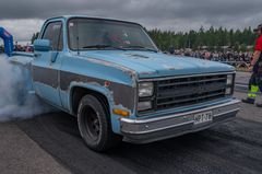 Sininen pickup-auto tekee burnoutia, eturenkaista nousee savua.