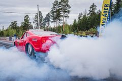 Punainen kilpa-auto aiheuttaa savua kiihdytyskilpailussa metsäisellä radalla.